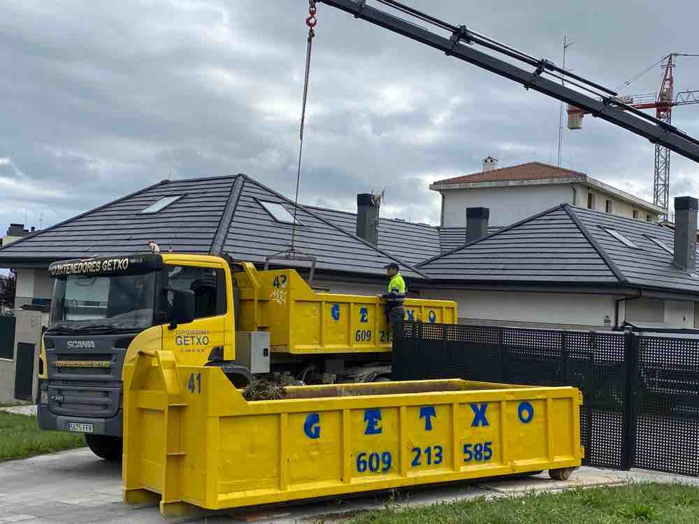 Contenedor amarillo número 41 de Contenedores Getxo colocado frente a una vivienda unifamiliar, con el camión y un operario con chaleco reflectante detrás